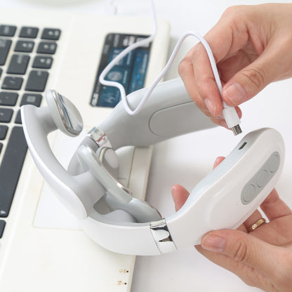 Hand holding a white and gray electronic neck massager with a laptop and card in the background