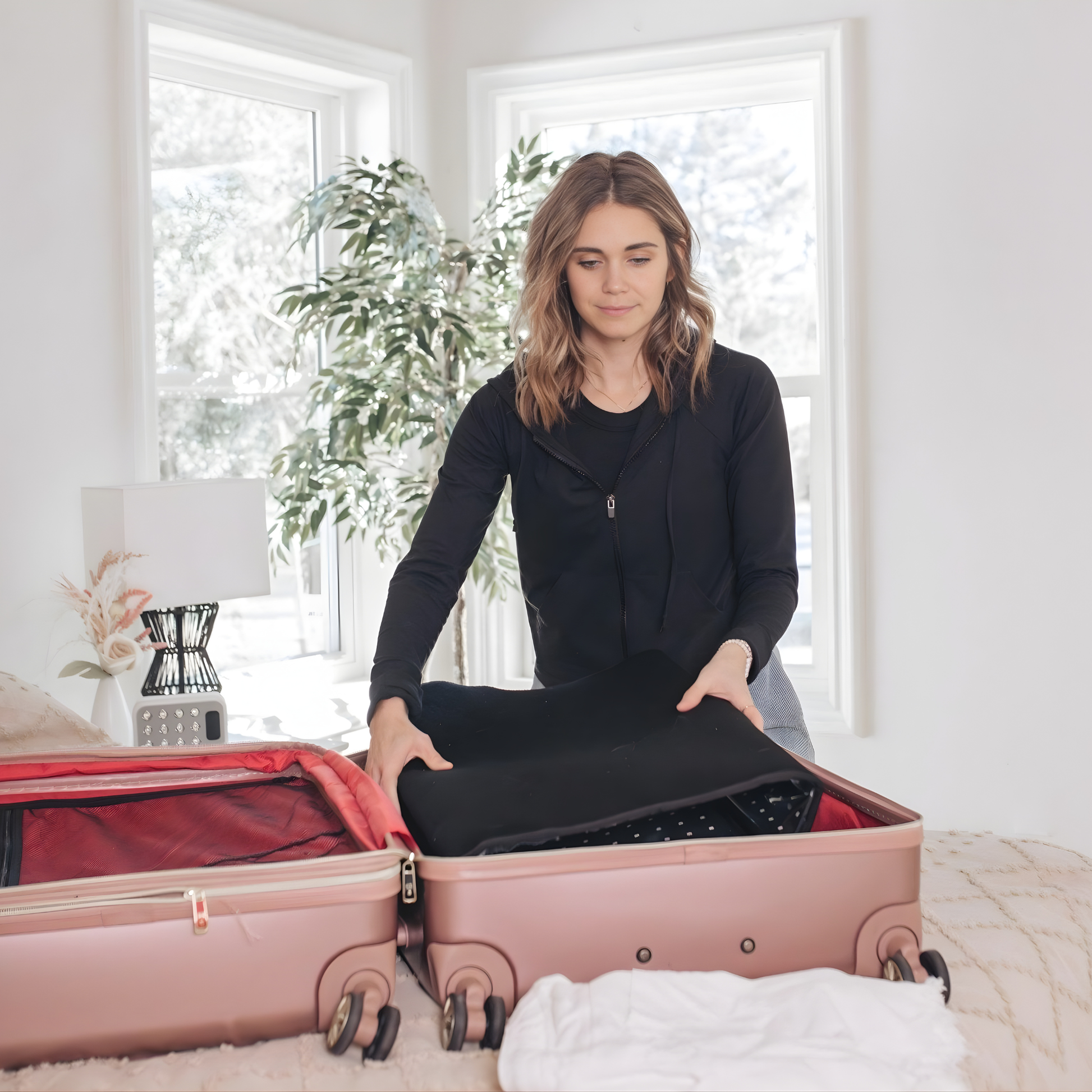 Woman packing a red light therapy mat into a suitcase in a bright room