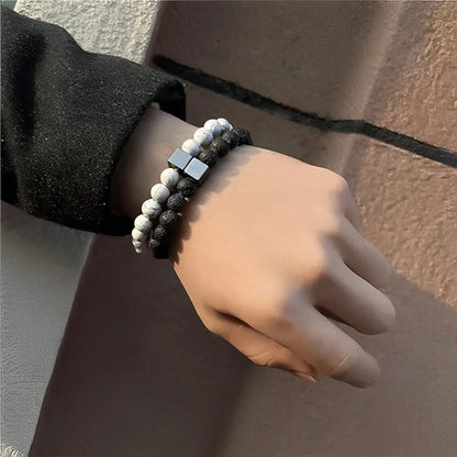Hand wearing 2 relaxation bracelets with black and white beads against a neutral background