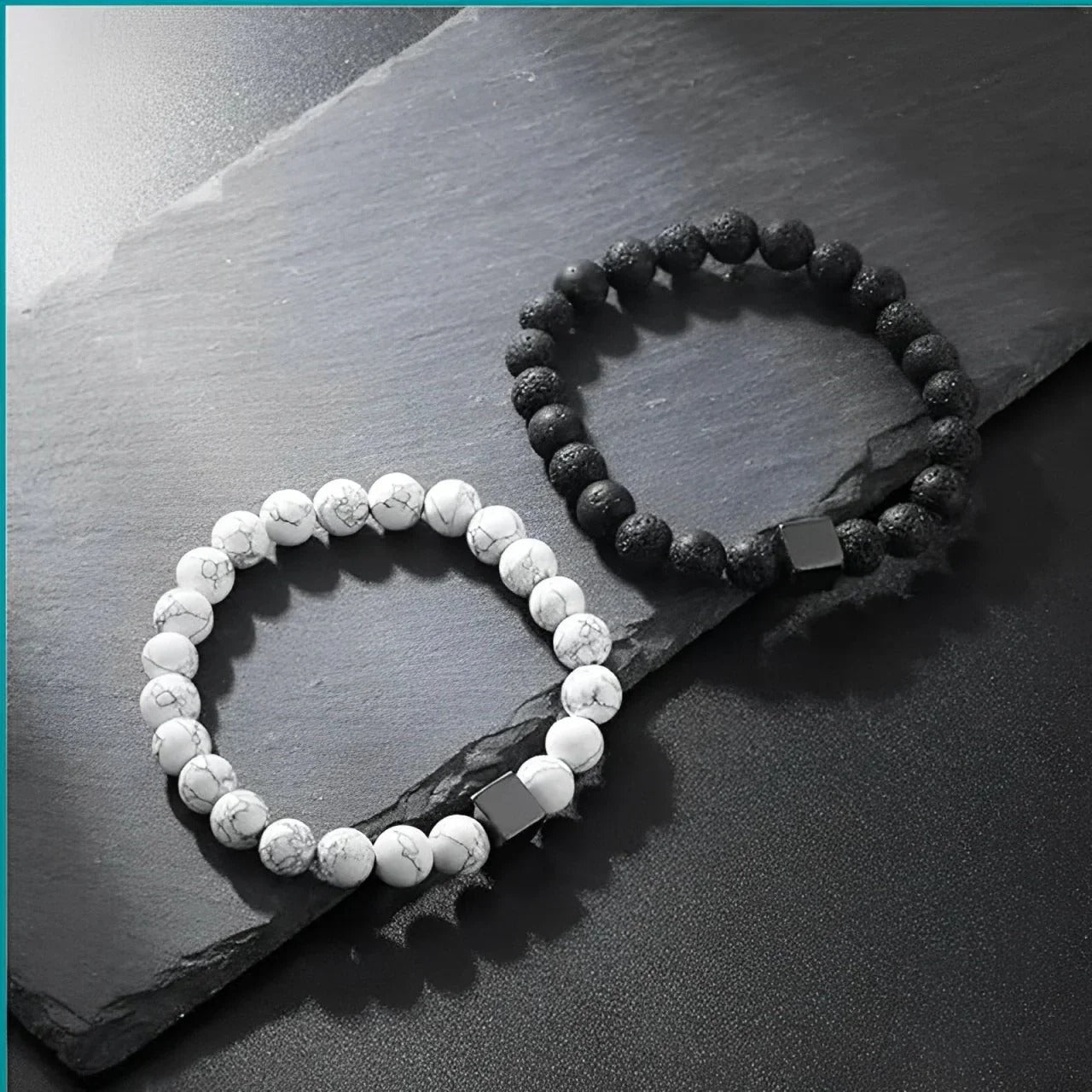 Two relaxation bracelets, one white and one black, on a dark slate surface.