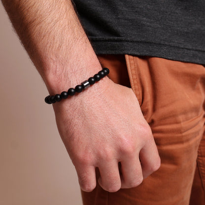 Person wearing a black relaxation bracelet on a neutral background
