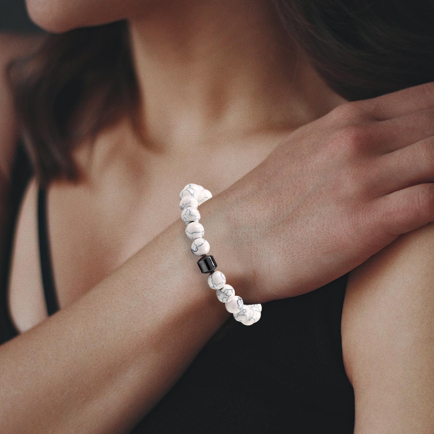 Close-up of a person wearing a white relaxation bracelet with a black bead on a blurred background
